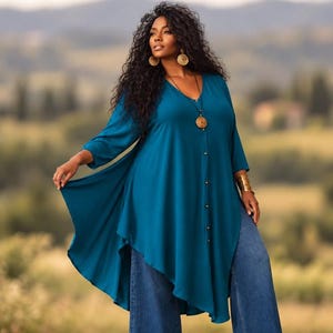 Puede incluir: Una túnica de color verde azulado con escote en V, mangas tres cuartos y cierre frontal de botones. La prenda presenta un dobladillo asimétrico que cae con soltura, combinada con pantalones vaqueros azules anchos y joyas doradas.