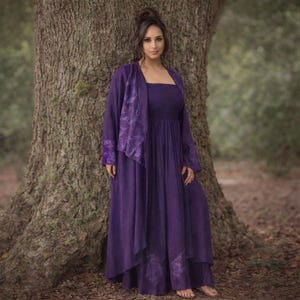 以下が含まれることがあります： 長い紫色の流れるようなドレスと、それに合うジャケットを着た女性。 ドレスはスクエアネックで、ウエストはギャザー入り。 ジャケットは長袖で、前面に装飾パネルが付いています。 この衣装は柔らかい生地で作られており、特別な機会に適しています。