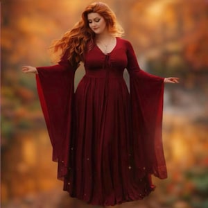 May include: A burgundy-colored dress with long, flowing sleeves and a V-neckline. The dress has a fitted bodice and a flared skirt, creating an elegant silhouette. The sleeves are wide and bell-shaped. The dress appears to be made of a soft, flowing fabric.