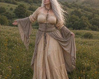Peut inclure: Robe beige et marron à épaules dénudées, avec de longues manches fluides et une jupe à volants. La robe présente une taille cintrée et un détail en tissu drapé. Le modèle se tient dans un champ de fleurs sauvages.