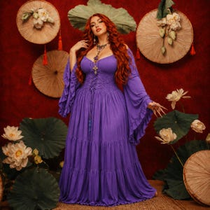 May include: A floor-length purple dress featuring long, flared sleeves, a corset-style lace-up bodice with a smocked waist, and a tiered skirt. The garment has a scoop neckline and is worn with a silver-toned pendant necklace with a cross charm.