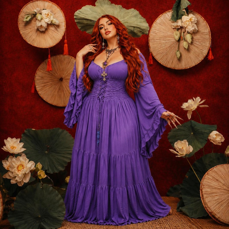 May include: A floor-length purple dress featuring long, flared sleeves, a corset-style lace-up bodice with a smocked waist, and a tiered skirt. The garment has a scoop neckline and is worn with a silver-toned pendant necklace with a cross charm.