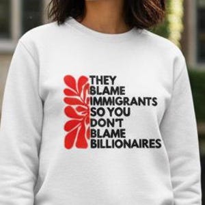 May include: White sweatshirt with the text "THEY BLAME IMMIGRANTS SO YOU DON'T BLAME BILLIONAIRES" in black and red. The sweatshirt has a crew neck and long sleeves. The graphic is on the front of the sweatshirt.