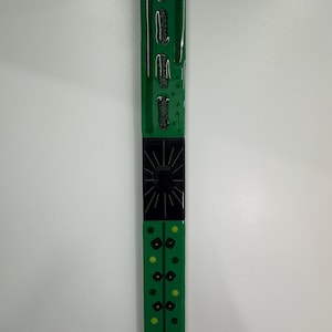 May include: A long, rectangular, green glass object with black and yellow accents. The top section has three black, curved shapes. The middle section is black with a sunburst design. The bottom section has yellow dots.
