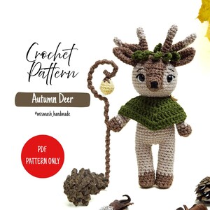 Może przedstawiać: Szydełkowa lalka Autumn Deer z zieloną peleryną i laską. Lalka ma brązowe rogi, jasnobrązową twarz i beżowe nogi. Widoczny jest tekst "Crochet Pattern" i "Autumn Deer".