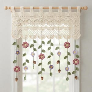 May include: A cream-coloured crochet valance hangs from a wooden rod, featuring an intricate scalloped lace top. Dangling from the bottom are several vertical green vines adorned with small pink and purple flowers and tiny brown acorns.