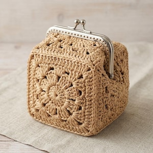 May include: A square-shaped crochet pouch crafted from light tan raffia-like yarn, featuring a prominent floral granny square pattern on the front and sides. The bag is secured with a silver-toned metal kiss-lock frame closure at the top.