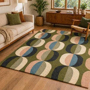 May include: A green area rug with a repeating pattern of overlapping ovals in shades of beige, pink, blue, and black. The rug is placed on a hardwood floor in a living room setting, with a sofa and wooden furniture visible.