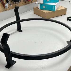Puede incluir: Un soporte circular de metal negro con tres patas de soporte. El soporte tiene una parte superior redonda y est&aacute; dise&ntilde;ado para sostener un objeto. El soporte es de metal y tiene un acabado mate.
