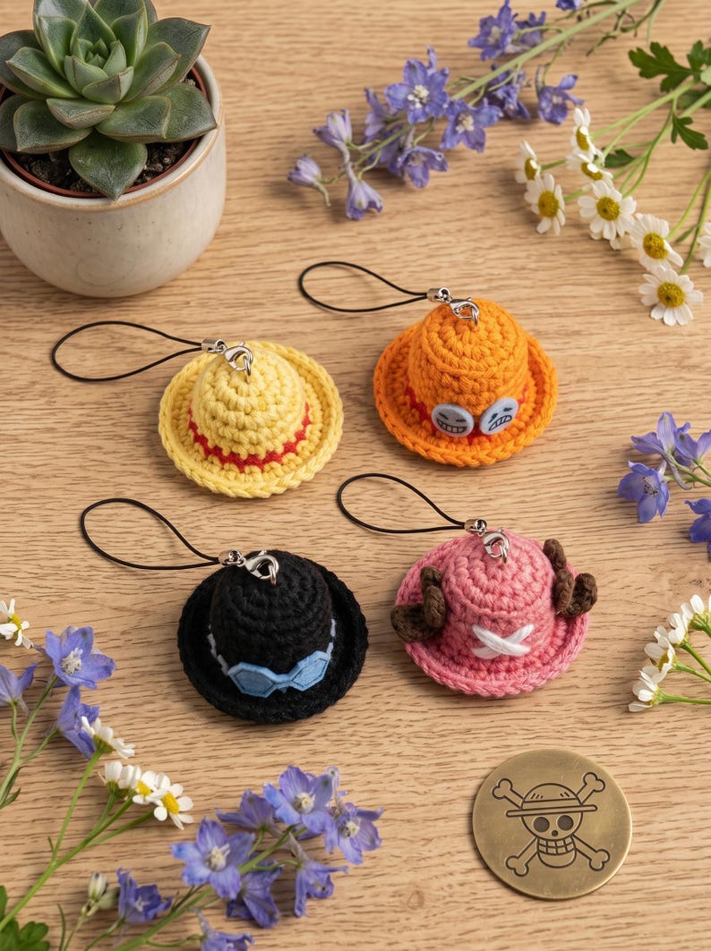 May include: Four miniature crocheted hats with black phone straps. One yellow hat with a red band, one orange hat with blue button accents, one black hat with blue goggles, and one pink hat with brown antlers and a white cross emblem.