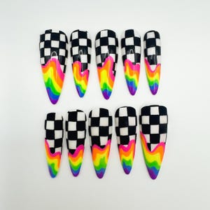 May include: A set of ten press-on nails featuring a black and white checkered pattern on the upper portion, transitioning into a vibrant, multi-coloured rainbow drip design at the tips. The nails have a pointed, almond-like shape with a glossy finish.