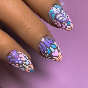 Op de afbeelding: Amandelvormige vingernagels met een textuurrijk, verhoogd patroon van abstracte vormen in tinten lavendel, lichtblauw, perzik en wit. De basis van de nagels is gedempt grijs en het ontwerp bedekt het gehele oppervlak van elke nagel.