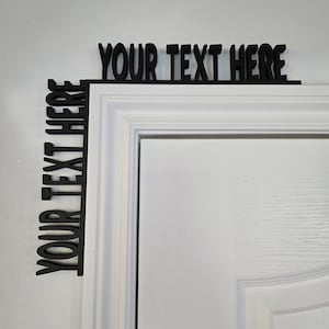 May include: Black wooden sign with the text "YOUR TEXT HERE" displayed on a white door frame. The sign is designed to wrap around the corner of the door frame, with text running horizontally and vertically.