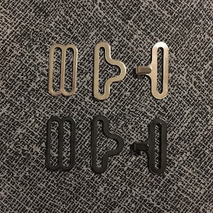 May include: Two sets of metal bra strap adjusters. One set is silver and the other is black.
