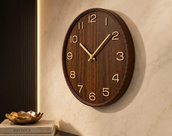 May include: A round wall clock featuring a dark brown wood grain face with raised gold-colored numerals and matching gold-colored hour, minute, and second hands. The clock has a circular frame in a matching dark brown wood finish.