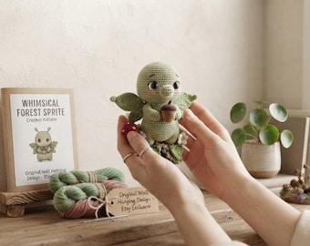 May include: A small, light green crocheted creature with large dark eyes, holding a brown acorn. Beside it sits a paper pattern booklet titled WHIMSICAL FOREST SPRITE, a small red mushroom, and two skeins of green and pink yarn with a paper tag.