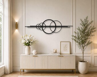May include: A black metal wall art piece featuring a horizontal arrangement of four interconnected circular rings and three parallel straight lines, creating a geometric design that spans across the wall surface in a linear composition.