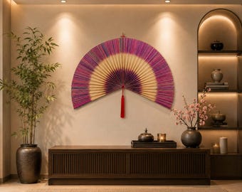 May include: A large, semi-circular wall-mounted folding fan featuring a gradient design that transitions from a deep purple outer edge to a light cream center. The fan is accented with a vibrant red tassel hanging from the central pivot point.