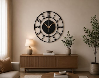 May include: A large circular wall clock featuring a black metal frame with open-work numerals and a solid black center disc. The clock has two thin gold-colored hands indicating the time, mounted against a plain wall above a wooden console table.
