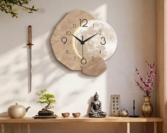 May include: A beige wall clock with a moon-shaped face and black hands. The clock is surrounded by a stone-like frame. The room also features a sword, bonsai tree, Buddha statue, and other decorative items.
