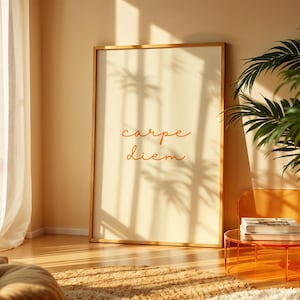 May include: A rectangular wall art print in a thin gold frame featuring the text carpe diem in a cursive orange font on a cream background. The print is displayed in a vertical orientation with a clean, simple design and clear typography.
