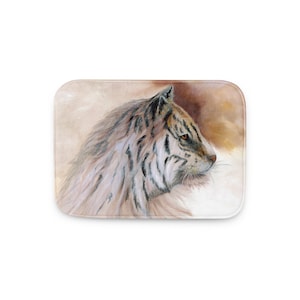 May include: A rectangular bath mat with a watercolour painting of a tiger's head in profile. The tiger has white fur with black stripes and orange eyes. The background is a blend of brown and beige.