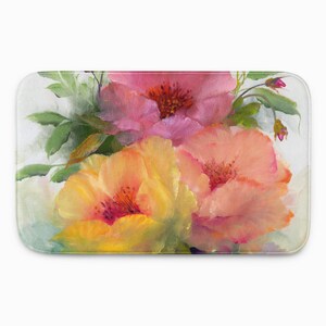 May include: A rectangular bath mat featuring a painterly floral design with large, vibrant blossoms in shades of pink, peach, and yellow. The flowers are accented by deep red centers and surrounded by soft green leaves on a light, neutral background.