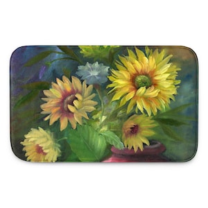 May include: A rectangular bath mat featuring a painted floral arrangement of bright yellow sunflowers and a single small white flower. The flowers are set in a dark red vase against a moody, blended background of deep blue, green, and brown tones.