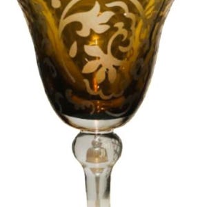 May include: An amber-colored wine glass with a clear stem and base. The bowl features an etched floral design. The glass has a bulbous stem and a wide, rounded base. The glass is likely made of crystal.