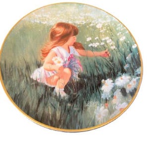 May include: Decorative plate featuring a young girl in a field of daisies. The girl, with auburn hair, is picking flowers. The plate has a gold rim and a pastoral scene with green grass and white flowers.