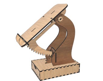 Op de afbeelding: Een houten telefoonstandaard met een tandwielmechanisme. De standaard is gemaakt van lichtbruin hout met donkerbruine accenten. Het heeft een lade voor het vasthouden van een telefoon en een basis met een kleine lade.