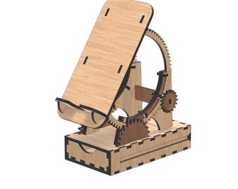 May include: A wooden phone stand with a gear mechanism. The stand is made of light brown wood and features a tilting platform, a gear system, and a small drawer. The design is intricate and appears to be laser-cut.