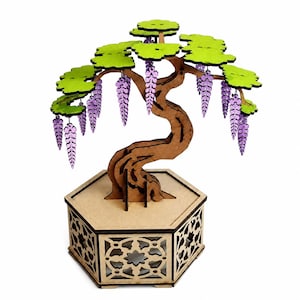 Puede incluir: Una escultura de madera cortada con láser de una glicinia con tronco marrón, follaje verde brillante y racimos de flores moradas colgantes. El árbol está montado sobre una base hexagonal con intrincados recortes geométricos en los paneles.