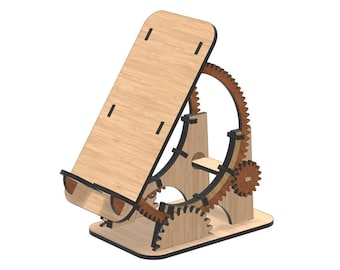 May include: A light-colored wooden phone or tablet stand featuring a mechanical gear-based adjustment system. The structure includes a flat rectangular support panel, a circular gear track, and smaller interlocking gears in dark wood.