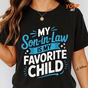 May include: Black t-shirt with the text "MY Son-in-Law IS MY FAVORITE CHILD" in white and blue. The shirt has a crew neck and short sleeves. The design is centered on the front.