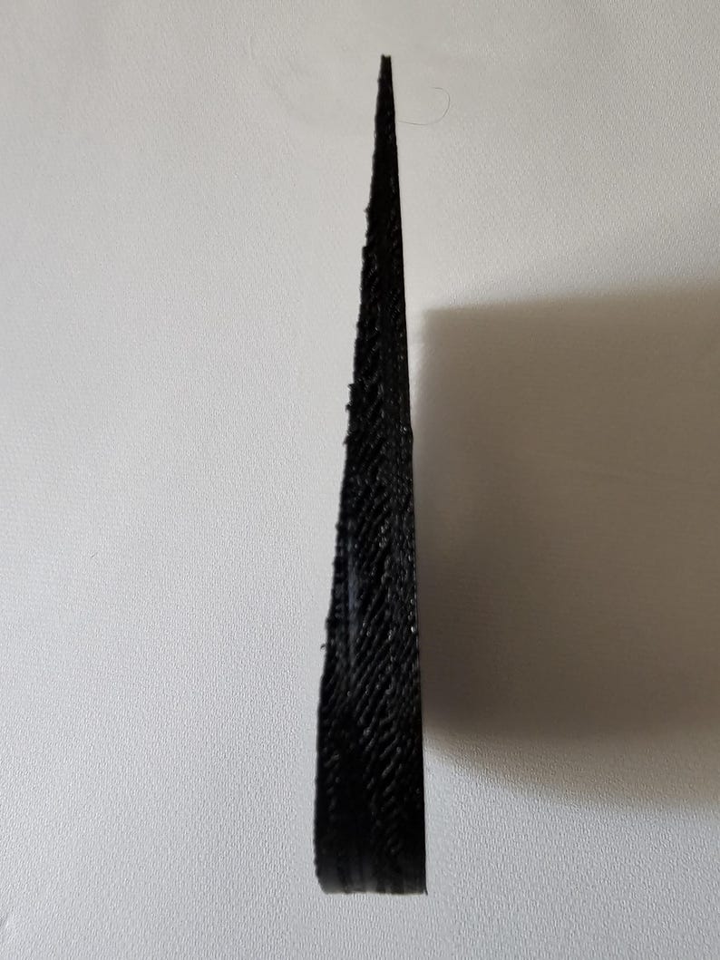 May include: A black, wedge-shaped object with a textured, layered surface. The item features a sharp, pointed tip at the top and a wider, flat base at the bottom, displaying a distinct 3D printed finish with visible horizontal lines throughout.