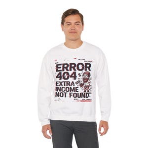 May include: White sweatshirt with a graphic that reads "ERROR 404 EXTRA INCOME NOT FOUND." The design includes a cartoon illustration of a man holding money. The text has a glitch effect.