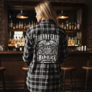 May include: Black and white plaid flannel shirt with a large graphic on the back. The graphic features the words "JOHNNY CASH" above an eagle and the words "MAN IN BLACK" and "NASHVILLE TENNESSEE".