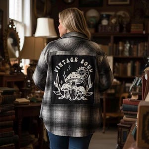 May include: A black and white plaid shirt jacket with a large black patch on the back. The patch features the words "VINTAGE SOUL" in a circular design, along with a graphic of mushrooms and a sun.