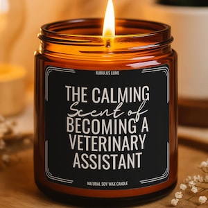 Puede incluir: Una vela encendida en un tarro de cristal color ámbar sobre una bandeja de madera. La vela tiene una etiqueta negra con texto blanco: "The Calming Scent of Becoming a Veterinary Assistant." La vela está etiquetada como "Natural Soy Wax Candle."