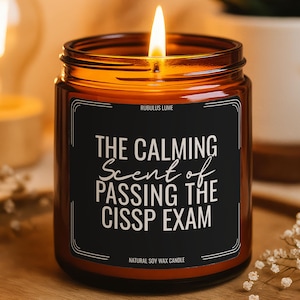 May include: A lit soy wax candle in a brown glass jar. The black label reads "THE CALMING Scent of PASSING THE CISSP EXAM". The candle sits on a wooden tray, with a blurred background of a light and a plant.