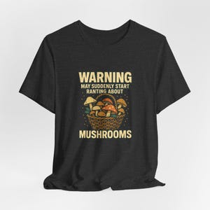 May include: Dark gray t-shirt with a graphic of a basket of mushrooms. The text on the shirt reads "WARNING MAY SUDDENLY START RANTING ABOUT MUSHROOMS". The mushrooms are brown, orange, and yellow.