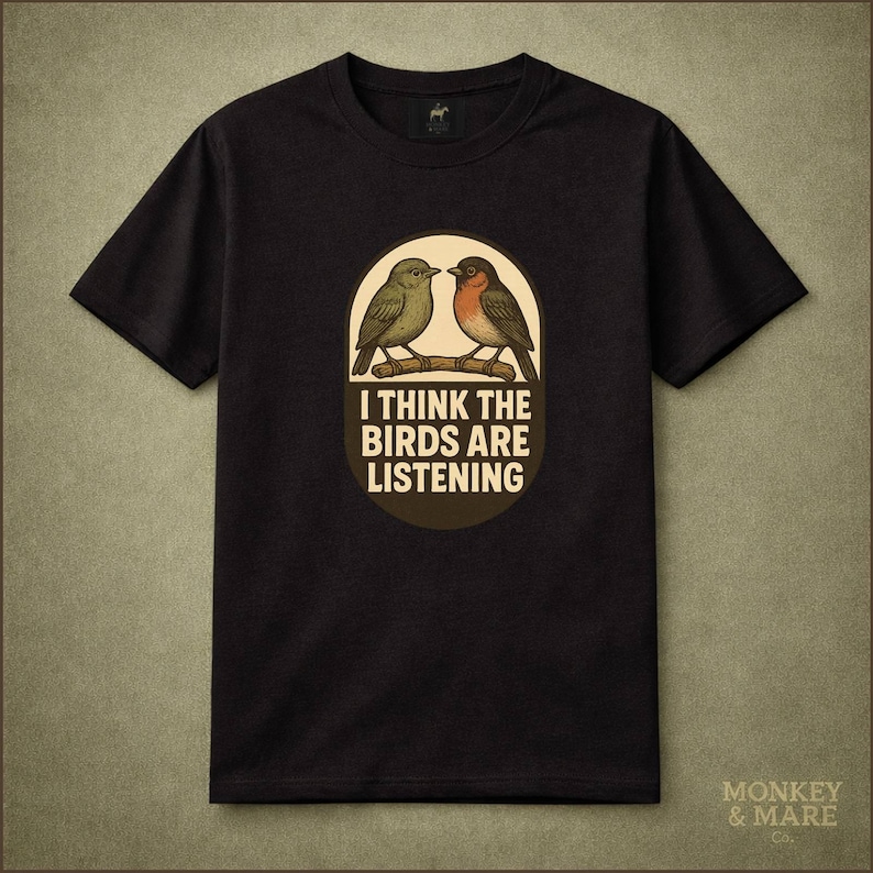May include: Black t-shirt featuring a graphic of two birds perched on a branch inside an oval. The text "I THINK THE BIRDS ARE LISTENING" is below the birds. The shirt has short sleeves and a crew neck.
