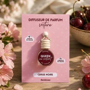 Op de afbeelding: Een kleine glazen autoparfumverspreider met een houten dop en ophangkoord, bevestigd op een roze kaart met de tekst DIFFUSEUR DE PARFUM voiture, QUEEN au volant, 10ML - CERISE NOIRE, PARFUM DE GRASSE, FABRIQUÉ EN FRANCE en de merknaam flambeuse.