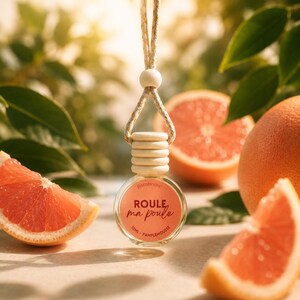 Peut inclure: Une petite bouteille ronde en verre avec un bouchon en bois et une ficelle pour suspendre. La bouteille porte une étiquette avec le texte "ROULE, ma poule" et "10ML - PAMPLEMOUSSE". L'arrière-plan comprend des tranches de pamplemousse et des feuilles vertes.
