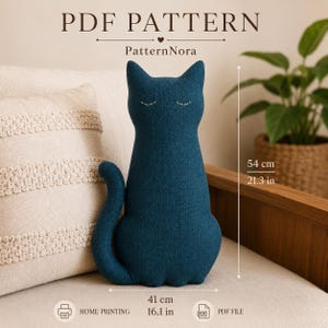 以下が含まれることがあります： 濃いティール色の布製猫型ぬいぐるみ。刺繍された閉じた目が特徴です。テキストには「PDF PATTERN」「PatternNora」、高さ54cm、幅41cmと記載されています。アイコンは家庭用プリンターでの印刷とPDFファイル形式を示しています。
