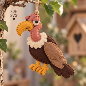 May include: A felt vulture ornament featuring a mustard yellow beak, a dusty rose head, a cream-colored scalloped neck ruff, and dark brown wings with light brown accents. The bird has yellow feet and hangs from a jute string. Text reads PDF SVG.
