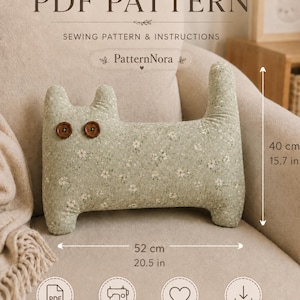 Può includere: Un cuscino di peluche a forma di gatto in tessuto verde chiaro con un piccolo motivo floreale bianco e due occhi a bottone marroni. Il cuscino misura 52 cm di larghezza per 40 cm di altezza. Il testo include PDF PATTERN, SEWING PATTERN & INSTRUCTIONS e PatternNora.