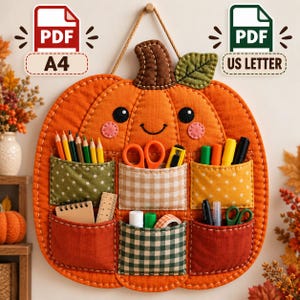 May include: A pumpkin-shaped fabric wall organizer featuring six pockets with various patterns including polka dots, gingham, and checks. The organizer holds colored pencils, scissors, a utility knife, markers, a small notebook, a ruler, and tape.