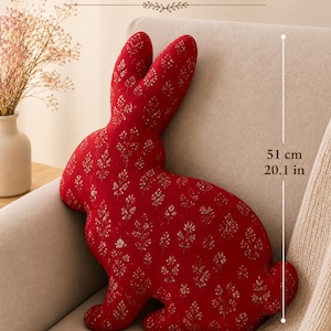 Può includere: Un cuscino a forma di coniglio rosso con un motivo floreale bianco ripetuto. Il cuscino misura 51 cm di altezza e 37 cm di larghezza. Il testo PDF PATTERN è visualizzato nella parte superiore dell'immagine, indicando un modello di cucito.